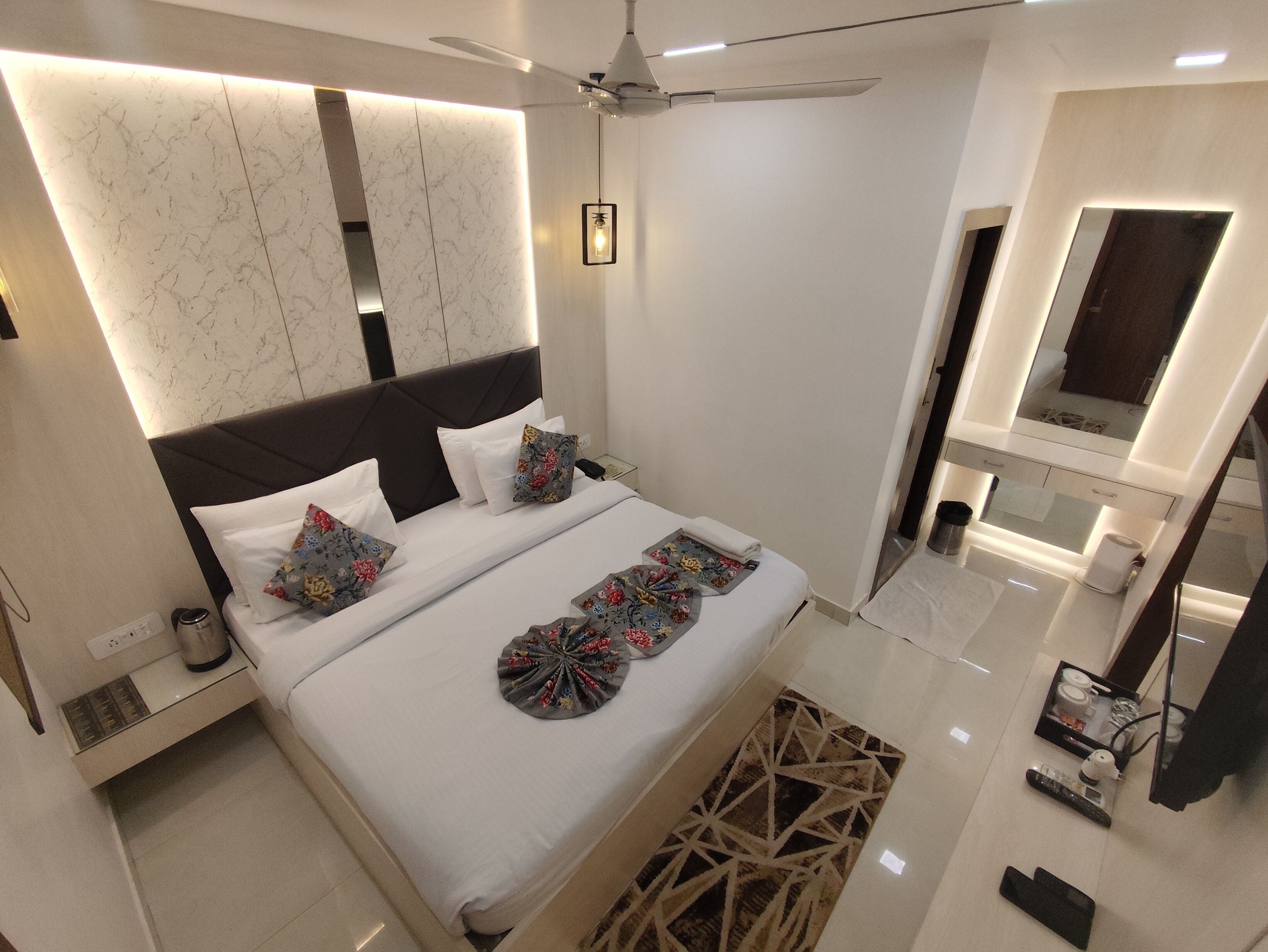 A modern hotel room with a large bed, a ceiling fan, a bathroom with a mirror, and a clean, minimalist design.