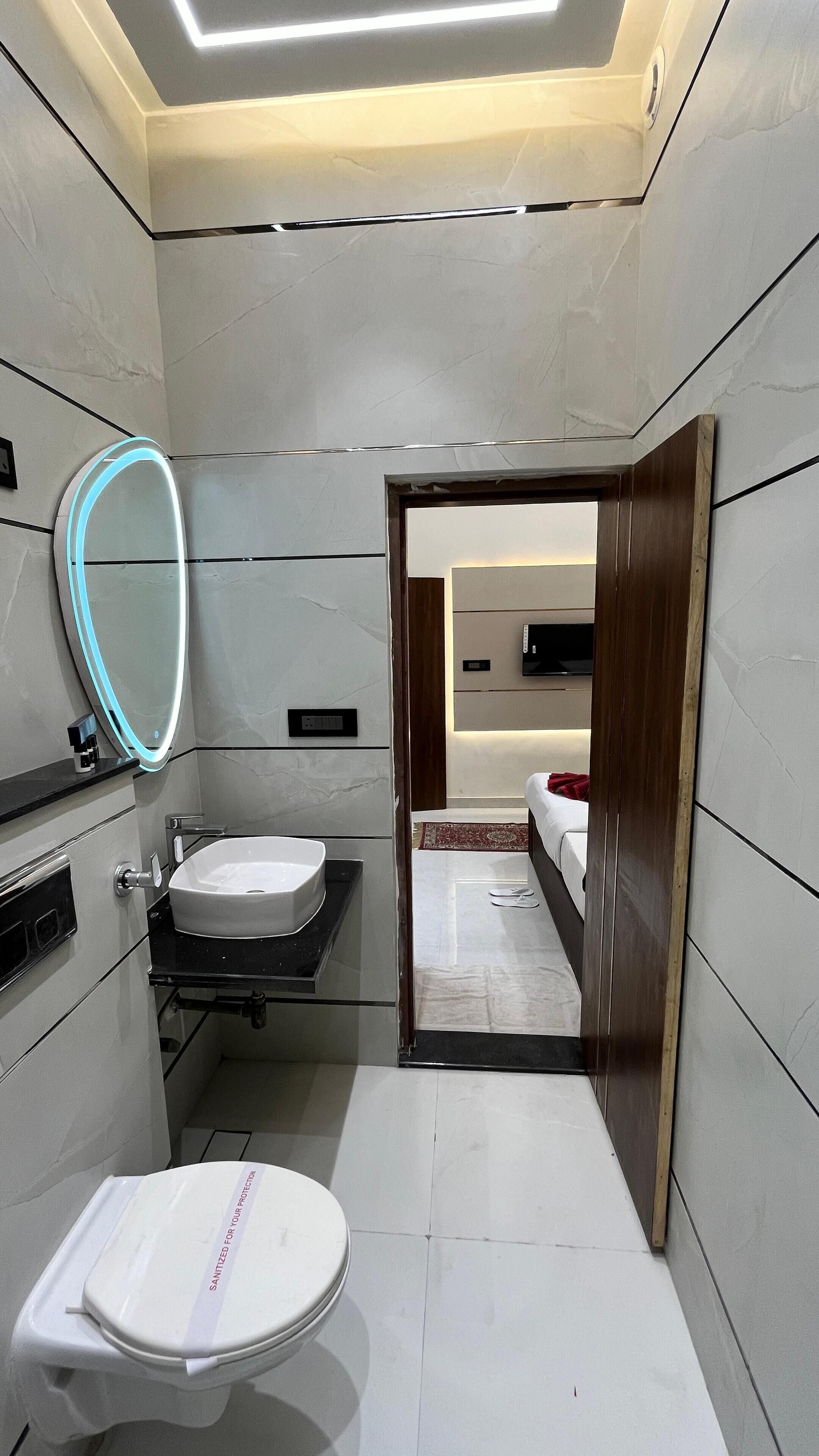 A modern bathroom with a toilet, sink, and mirror. There is a wooden door leading to a bedroom.