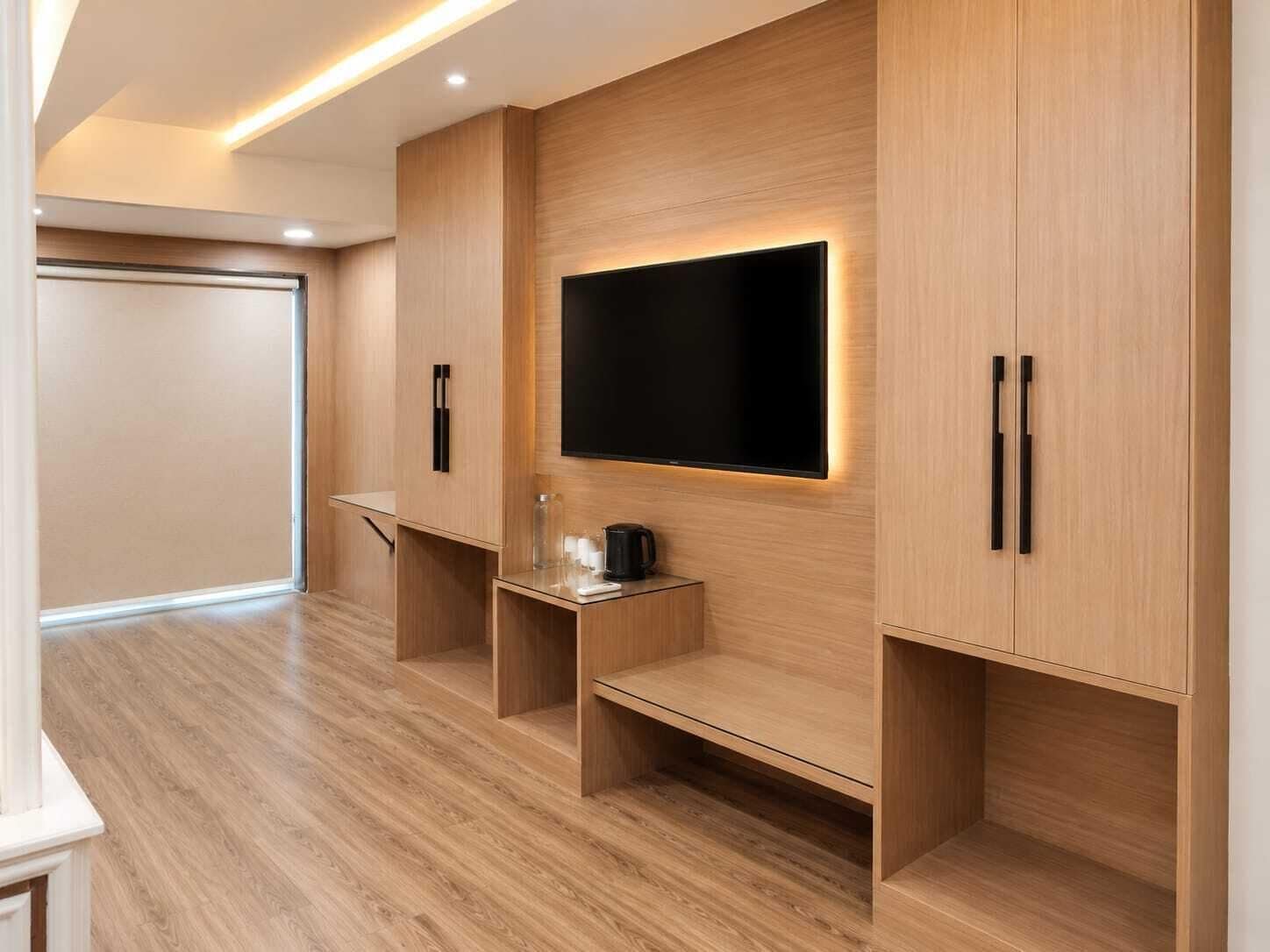Una moderna camera d'albergo con televisore piatto a parete, mobili in legno e un tavolino con una caffettiera.
