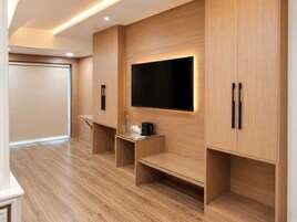 Une chambre d’hôtel moderne dotée d’un téléviseur à écran plat fixé au mur, de meubles en bois et d’une petite table avec une cafetière.