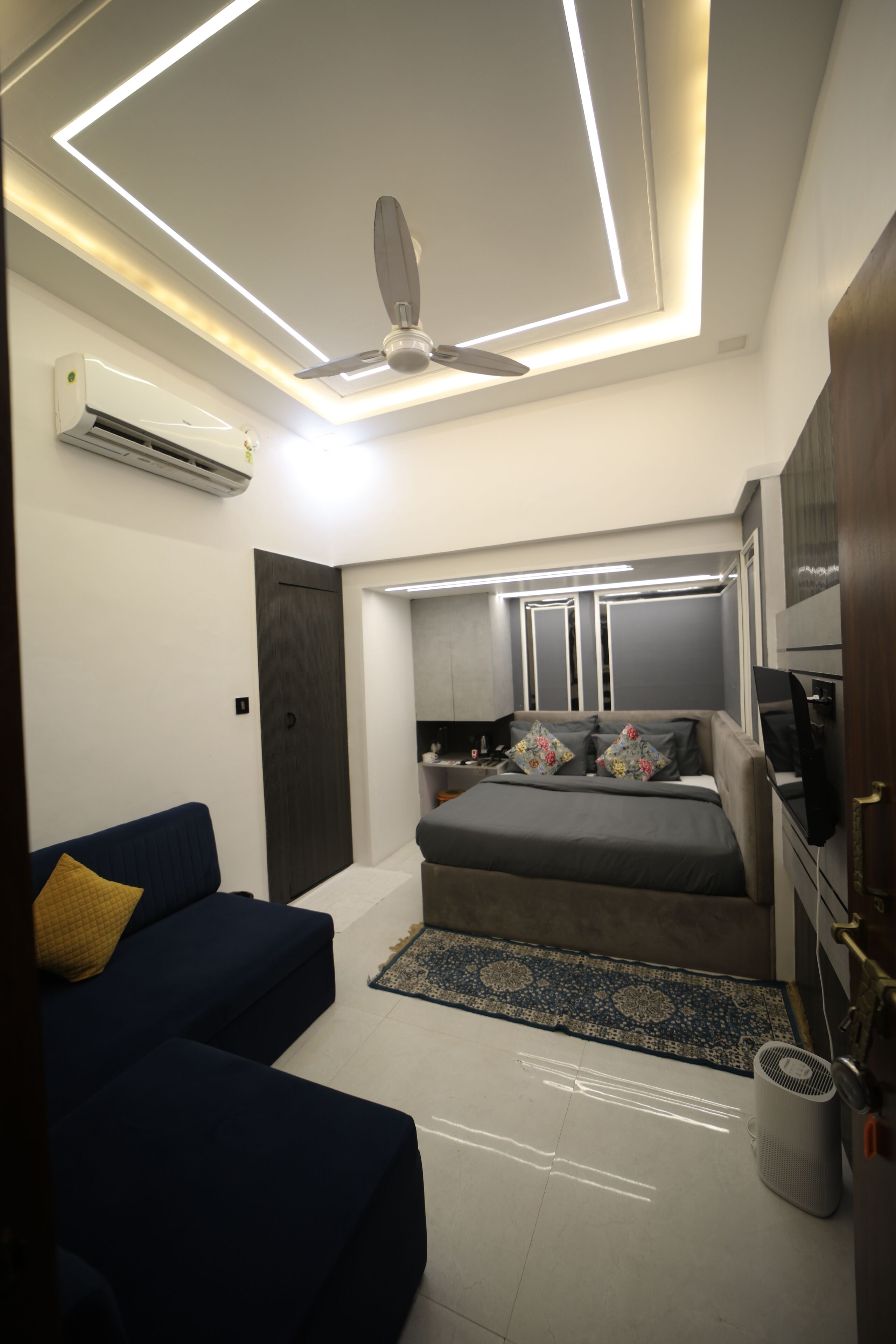 Une chambre moderne avec un lit, un ventilateur de plafond, un climatiseur, une télévision et un canapé bleu.