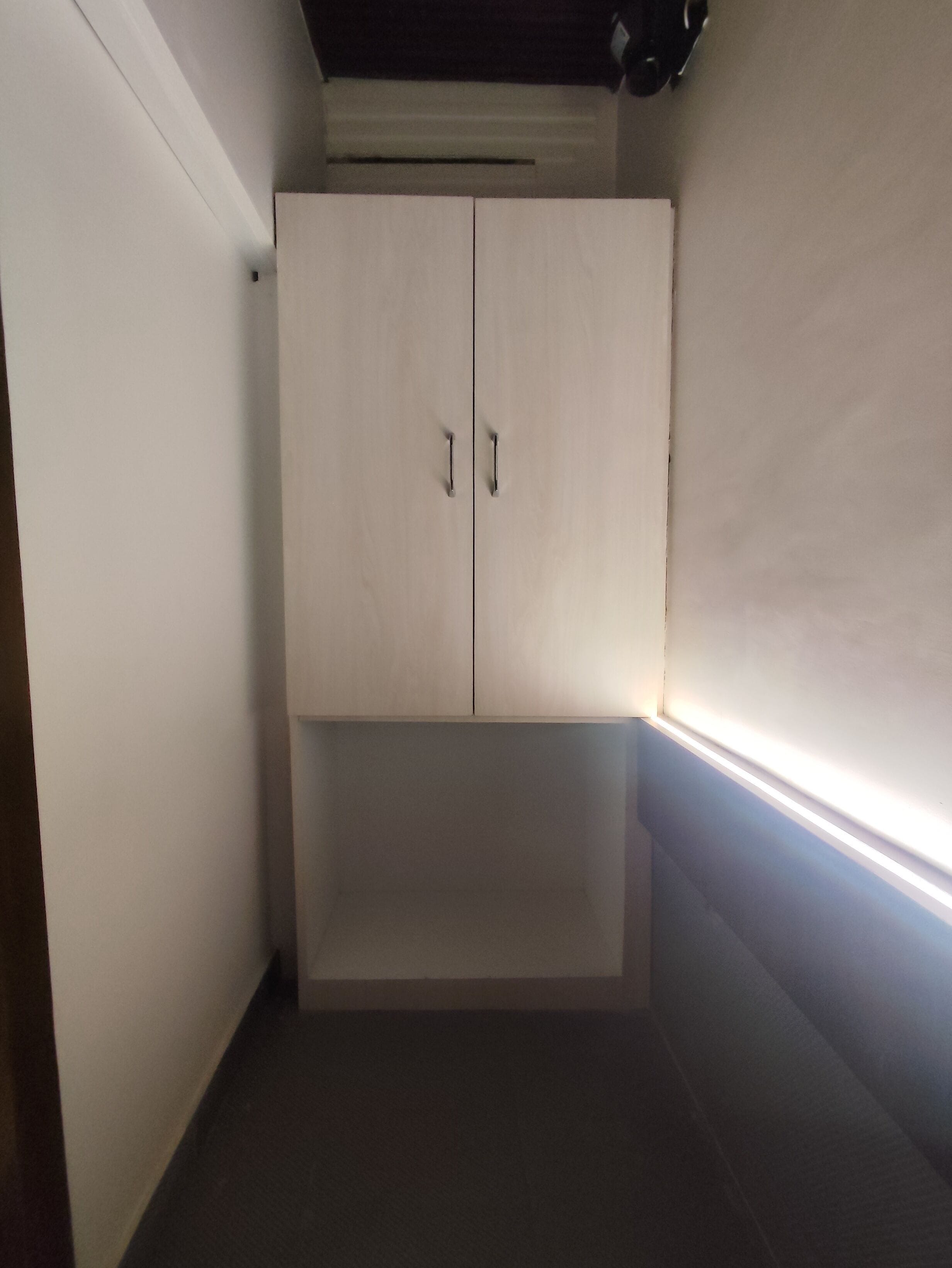 A small, narrow room with a white wardrobe and a light switch on the wall.