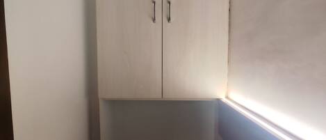 A small, narrow room with a white wardrobe and a light switch on the wall.