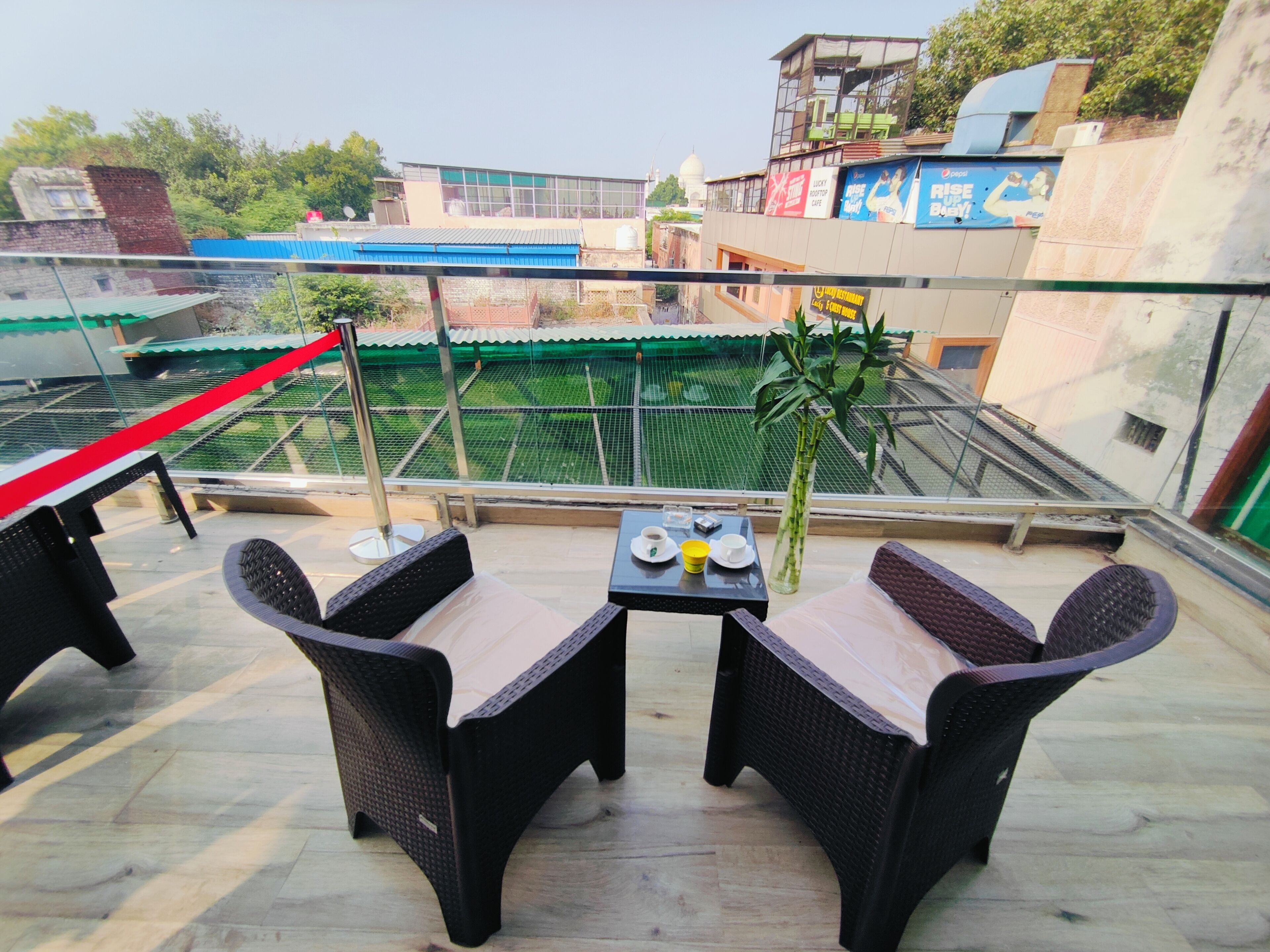 Una terraza con mobiliario de mimbre y una mesa, con vistas a un área verde y un edificio blanco al fondo.