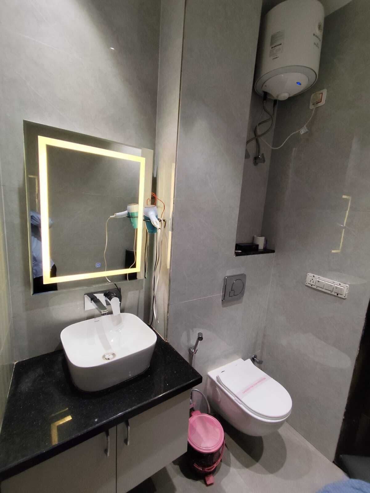 A modern bathroom with a white sink, a toilet, and a mirror with a lighted frame.