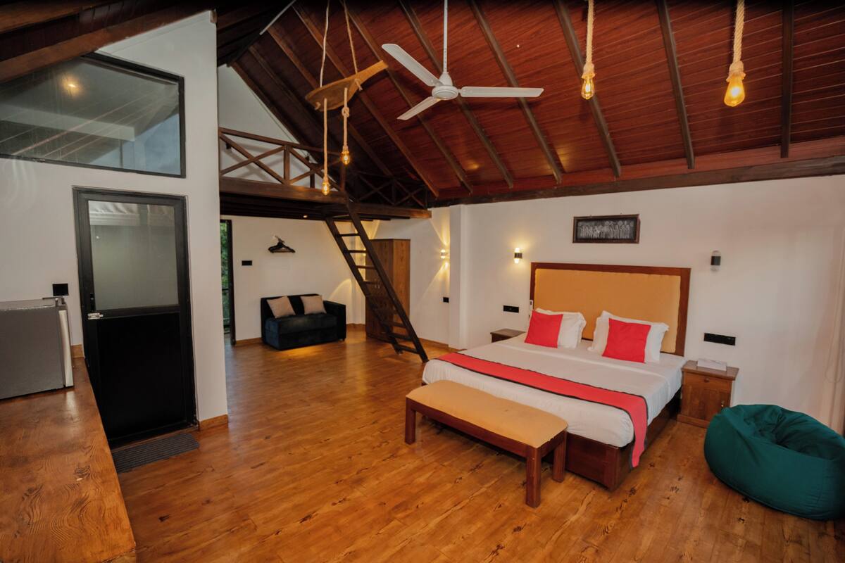 A spacious bedroom with a large bed, wooden flooring, a ceiling fan, and a view of the outdoors.