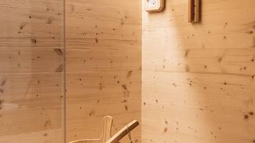 Una sauna de madera con un banco de madera, un cubo de madera y un mazo, y un panel de control de la sauna fijado a la pared.