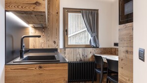 Une cuisine de taille réduite avec un mur d’accent en bois, un évier noir et une fenêtre agrémentée de rideaux.