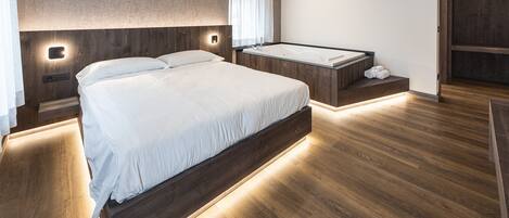 Un dormitorio moderno con una cama grande, una bañera integrada y suelo de madera.