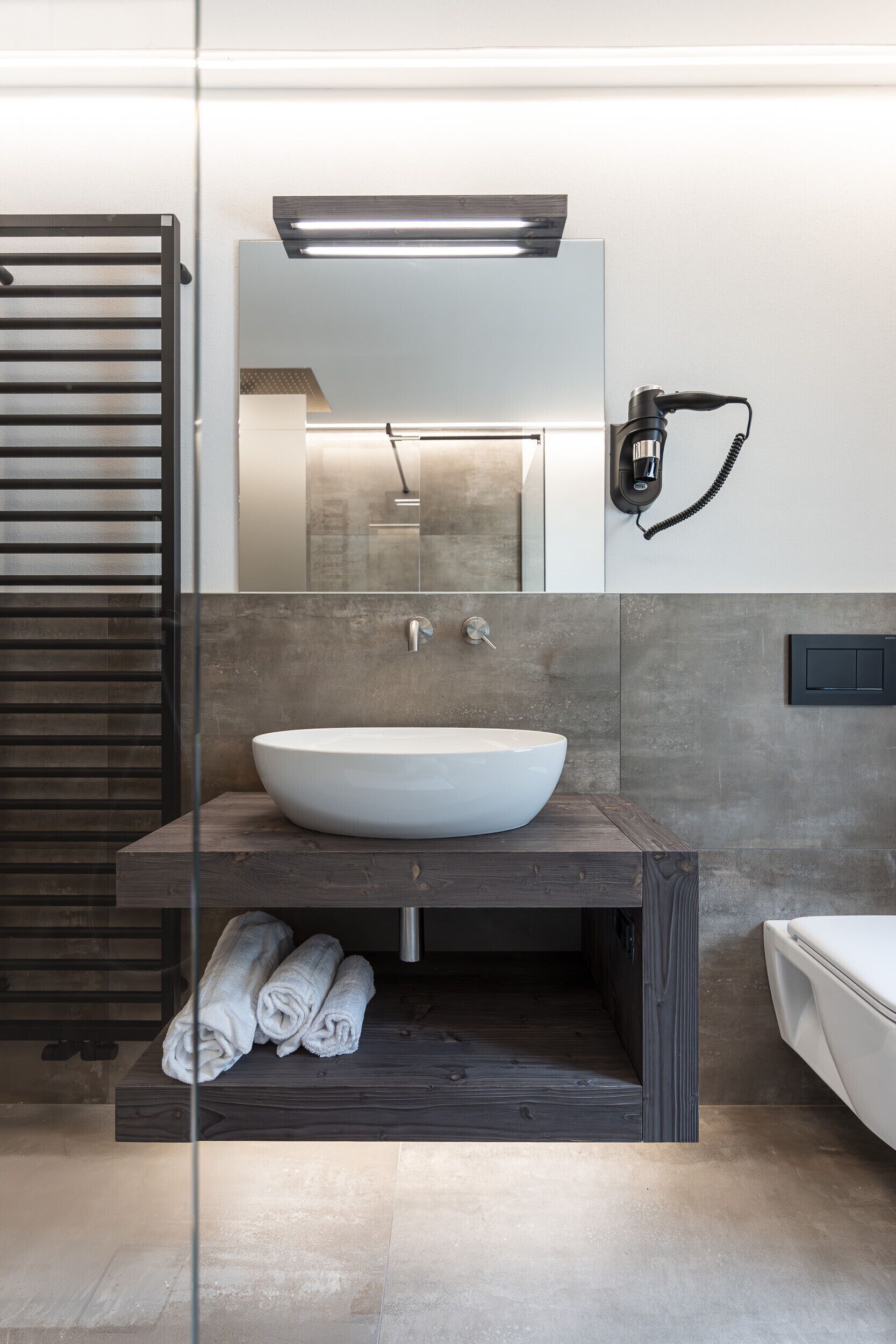 Une salle de bain moderne avec un grand lavabo sur pied, un meuble-lavabo en bois, une douche en verre et un porte-serviettes.