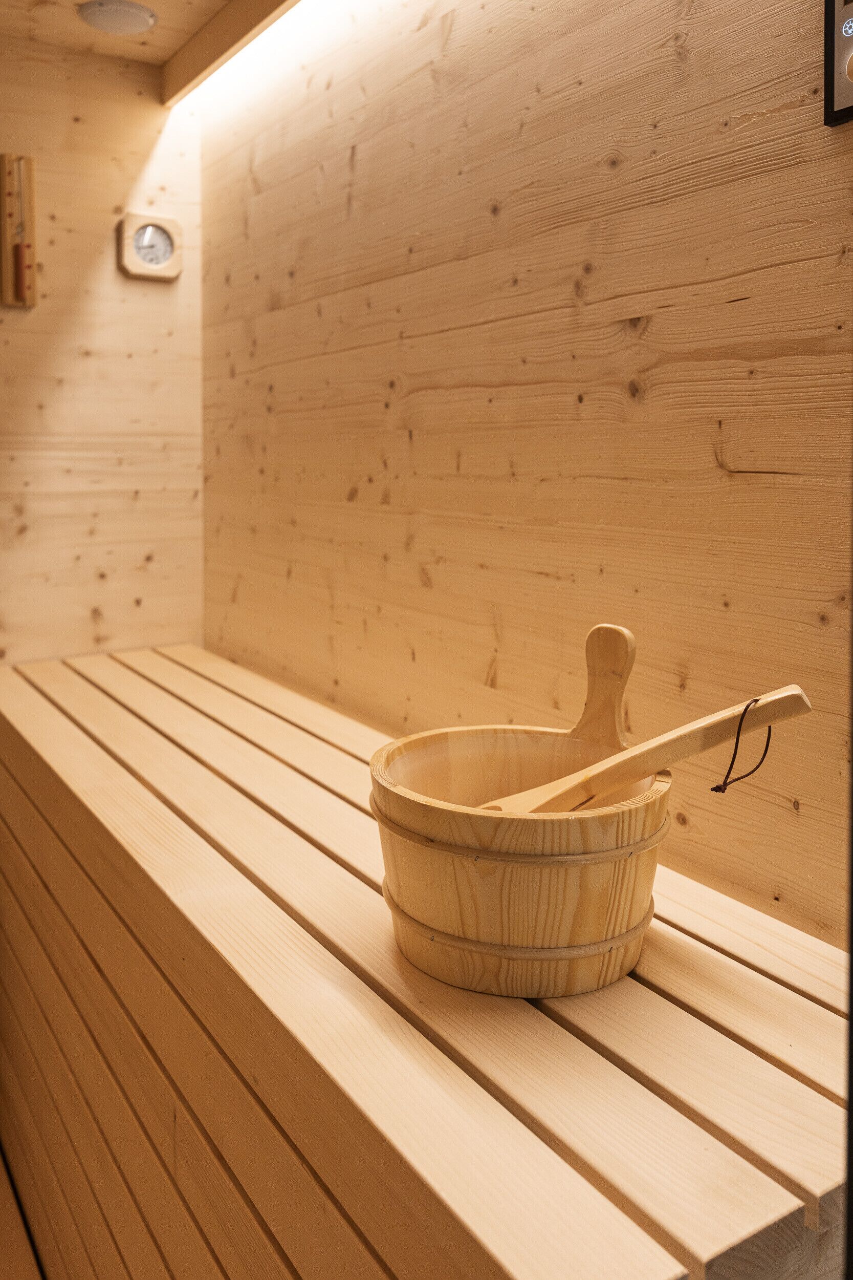 Un banc de fusta amb un cubet i un mall de fusta a la sauna.
