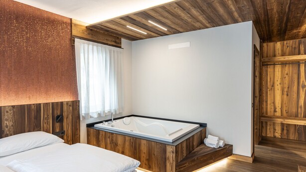 Ein modernes Schlafzimmer mit einem Holzkopfteil, einem großen Bett mit weißer Bettwäsche, einer integrierten Badewanne und Holzdielen.
