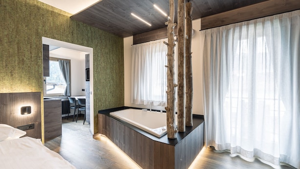 A modern bathroom with a wooden vanity, a bathtub, and a large window with sheer curtains.