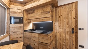A compact kitchen with wooden cabinetry, a built-in microwave, and a sink. - Salvans Wellness - Aurum Room (Auronzo di Cadore)
