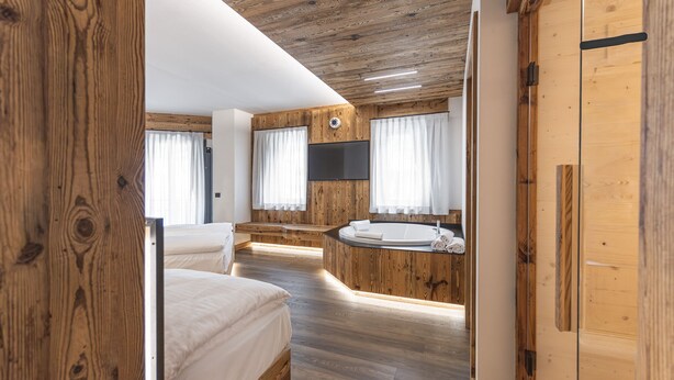 A bedroom with a wooden floor, a bed, a built-in bathtub, and a TV mounted on the wall. - Salvans Wellness - Aurum Room (Auronzo di Cadore)