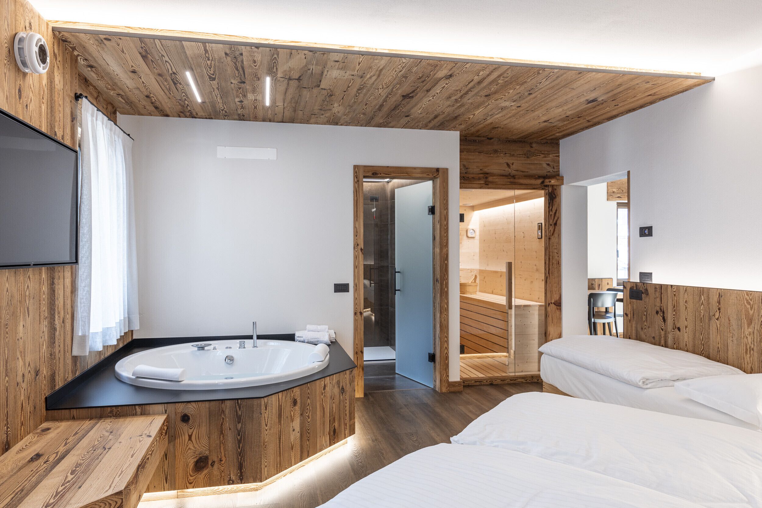 Ein modernes Hotelzimmer mit Holzbalkendecke, einer großen Badewanne, zwei Betten und einer Duschkabine.