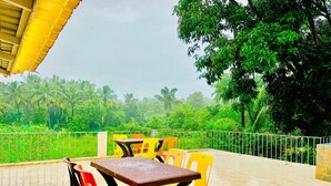 A terrace with a table and chairs, surrounded by a metal railing and lush greenery.