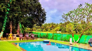 A swimming pool with a green artificial turf border, surrounded by trees and a green wall.
