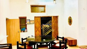 A dining area with a round glass table surrounded by chairs, a ceiling fan, and a staircase leading to an upper level.