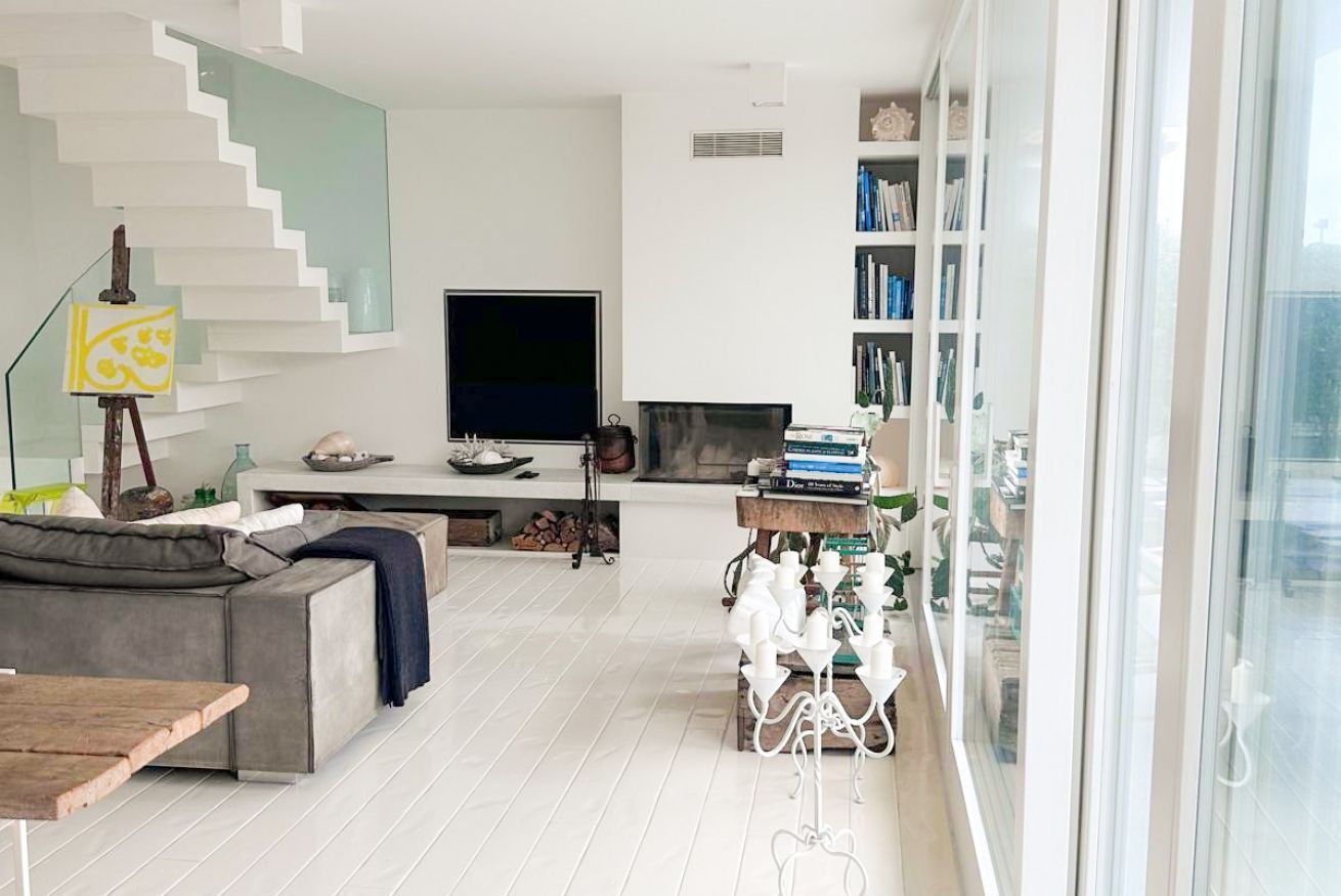 A modern living room with a grey sectional sofa, a flat-screen TV, a staircase, and a bookshelf.