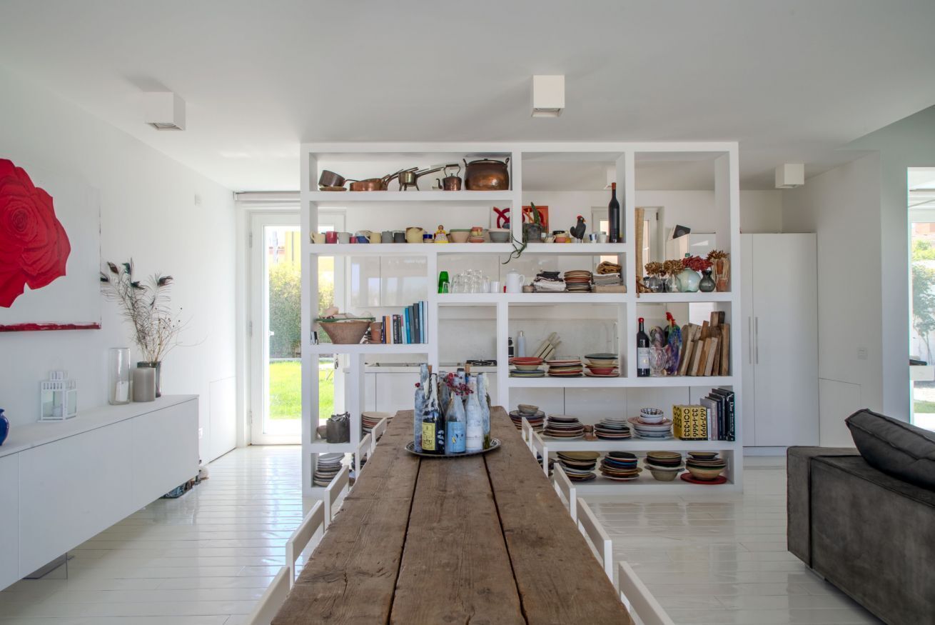 Une cuisine moderne avec des meubles blancs, une table à manger en bois et une variété d’ustensiles de cuisine et d’objets décoratifs.