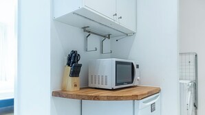 Cozinha compacta com micro-ondas em bancada de madeira, porta-facas e armário pequeno.