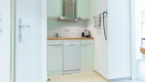 Uma cozinha compacta com lava-louças, exaustor de aço inoxidável e bancada pequena.