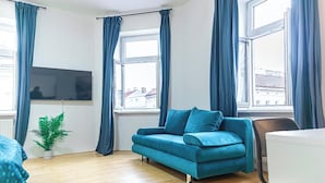 Um quarto com um sofá azul-turquesa, uma pequena planta em vaso e uma TV na parede.