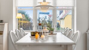 Ein Essbereich mit einem weißen Tisch und Stühlen, Kerzen und einer Pendelleuchte.