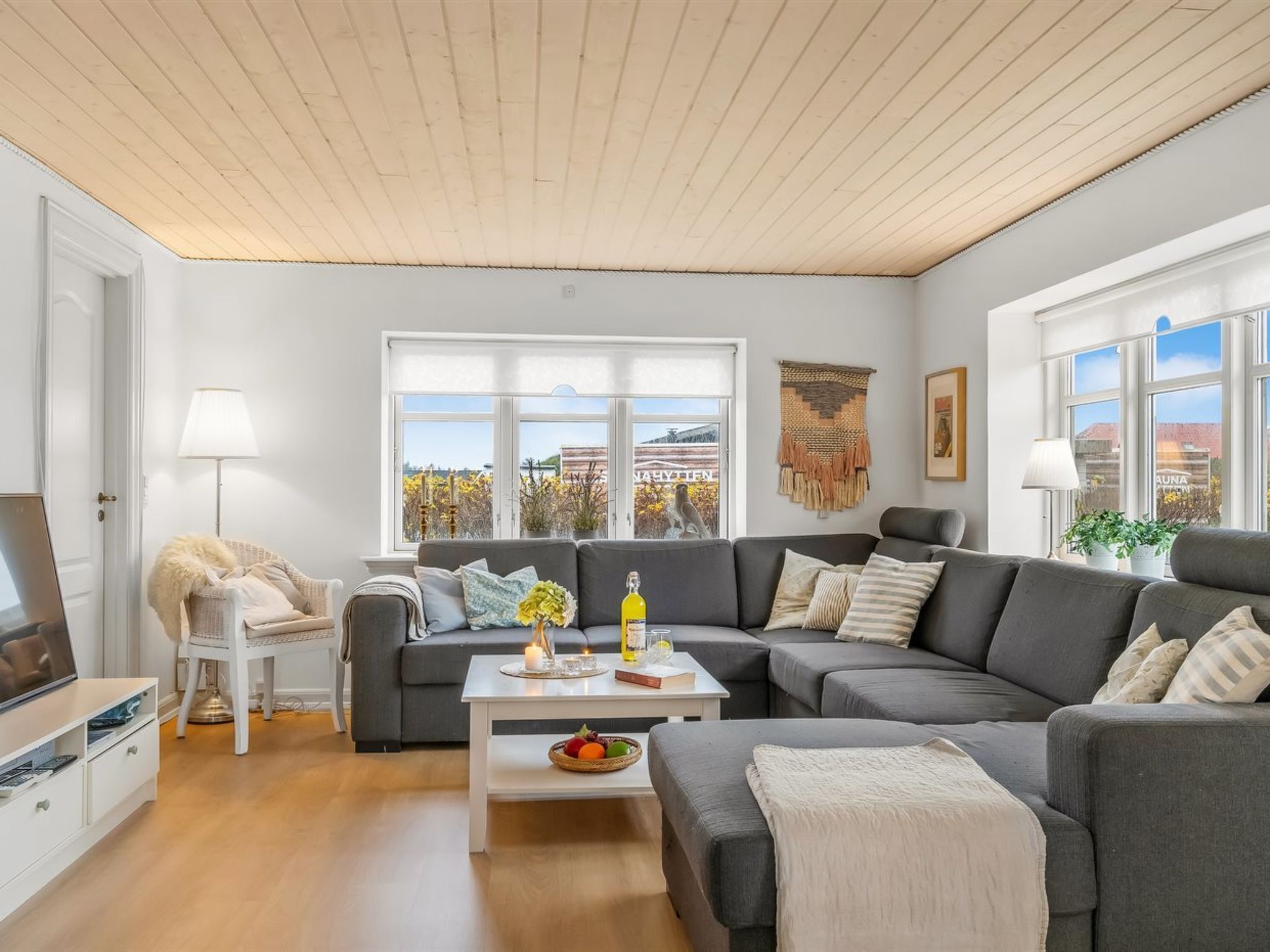 Una sala de estar moderna con un sofá gris, una mesa de centro blanca con una vela y vistas al exterior a través de ventanas amplias.