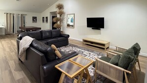 Ein modernes Wohnzimmer mit einem schwarzen Ledersofa, einem Couchtisch aus Holz, einem Korbstuhl und einem flachbildfernseher an der Wand.