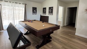 Ein geräumiges Zimmer mit Billardtisch, Billardkugeln und einem bequemen Sessel.