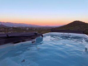 Uma banheira de hidromassagem com vista para uma cidade e montanhas ao pôr do sol.