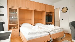 Une chambre avec deux lits, des armoires en bois, un bureau et une horloge au mur.