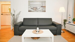 Un salon moderne avec un canapé en cuir noir, une table basse blanche et un tableau représentant un phare accroché au mur.