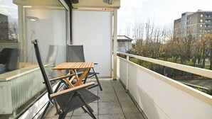 En balkon med bord og stole, en radiator samt udsigt til bygninger og træer.