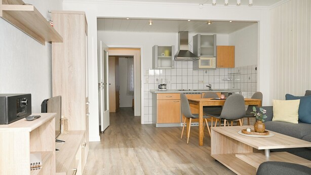 Et moderne køkken med træskabe, et spiseområde med bord og stole, og en stue med en sofa.
