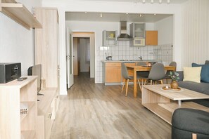 A modern kitchen with wooden cabinets, a dining area with a table and chairs, and a living room with a sofa. - Bright vacation apartment in Knütt (Büsum)