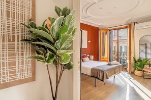 Una habitación de hotel moderna con cama, una planta grande en maceta, suelo de madera y vista a la ciudad por la ventana.