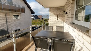 Ein Balkon mit Tisch und Stühlen, ein Fenster und Blick auf umliegende Gebäude.