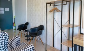 Una habitación moderna con un sofá de estampado blanco y negro, dos sillas negras, una mesita de madera y un estante de metal con un perchero de madera.