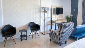 Una habitación de hotel moderna con sofá, dos sillones, televisor, escritorio y lámpara colgante.