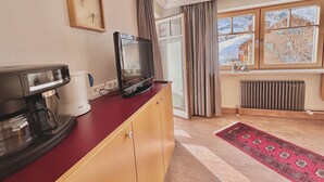 Una habitación con un armario de madera, una cafetera, un televisor y una ventana con vistas a un paisaje nevado.