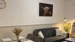 Uma sala de estar moderna com uma mesa de jantar de vidro, sofá cinzento e um quadro de um touro.