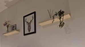 Quarto com cama, abajur, quadro de veado e duas prateleiras fixadas na parede com objetos decorativos.