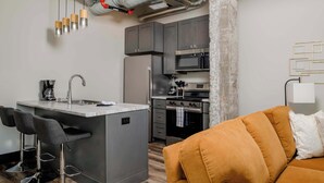 Une cuisine moderne avec des meubles gris, un îlot central intégré doté de tabourets, des appareils en acier inoxydable et un système de conduits apparent.