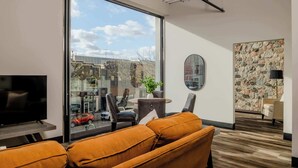 Un salon moderne doté d’une grande fenêtre, d’un ventilateur de plafond, d’un téléviseur à écran plat et d’un mur en pierre.