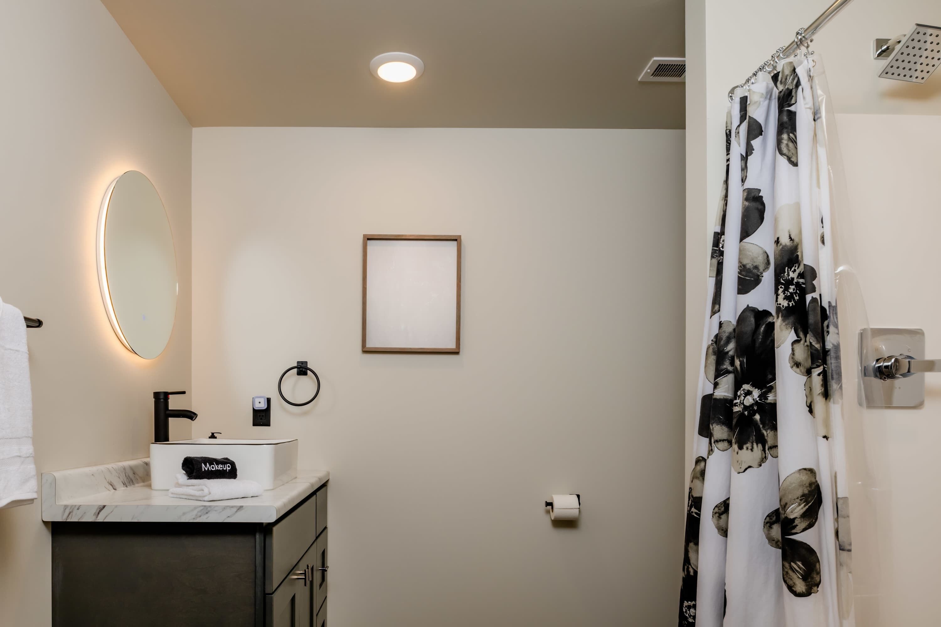 A bathroom with a marble sink, a black faucet, a framed picture on the wall, a toilet paper holder, and a shower curtain with a floral pattern.