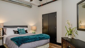 Une chambre à coucher comprenant un lit, des tables de chevet, un ventilateur de plafond, une armoire et une plante en pot.