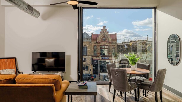Un salon moderne doté d’une grande fenêtre, d’un téléviseur à écran plat, d’un ventilateur de plafond et d’un coin repas avec des chaises et une table.